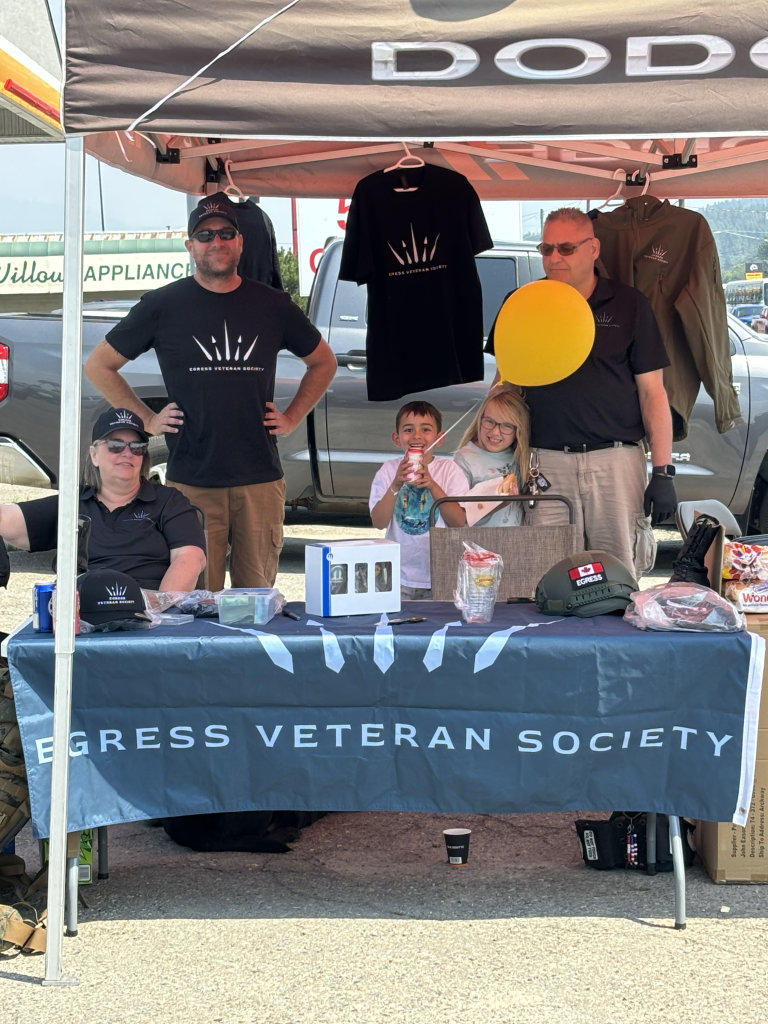 Members of the Egress Veteran Society hosting an outreach booth at a community event, featuring branded merchandise, informational materials, and smiling children engaging with the display.